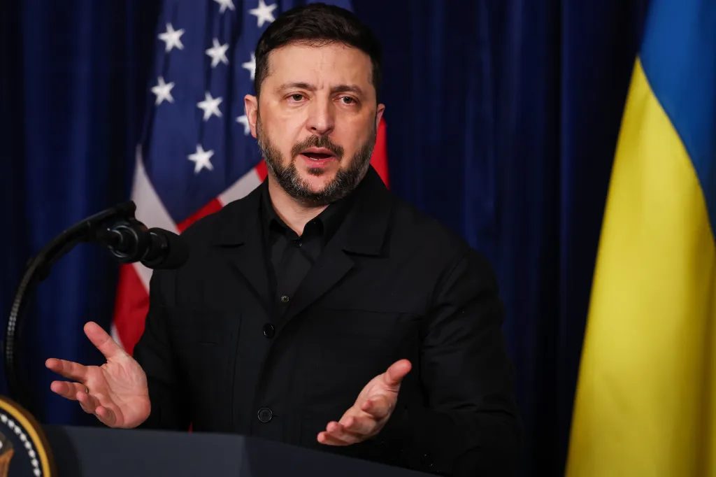 Ukrainian President Volodymyr Zelenskyy speaking at a press conference with the US and Ukrainian flags in the background.