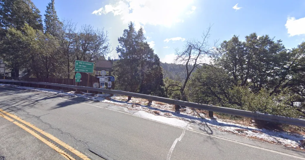 Street view of CA-138 and Crestline Road in Crestline, with a road sign indicating directions to Valley of Enchantment, Lake Gregory, and Cedarpines Park.