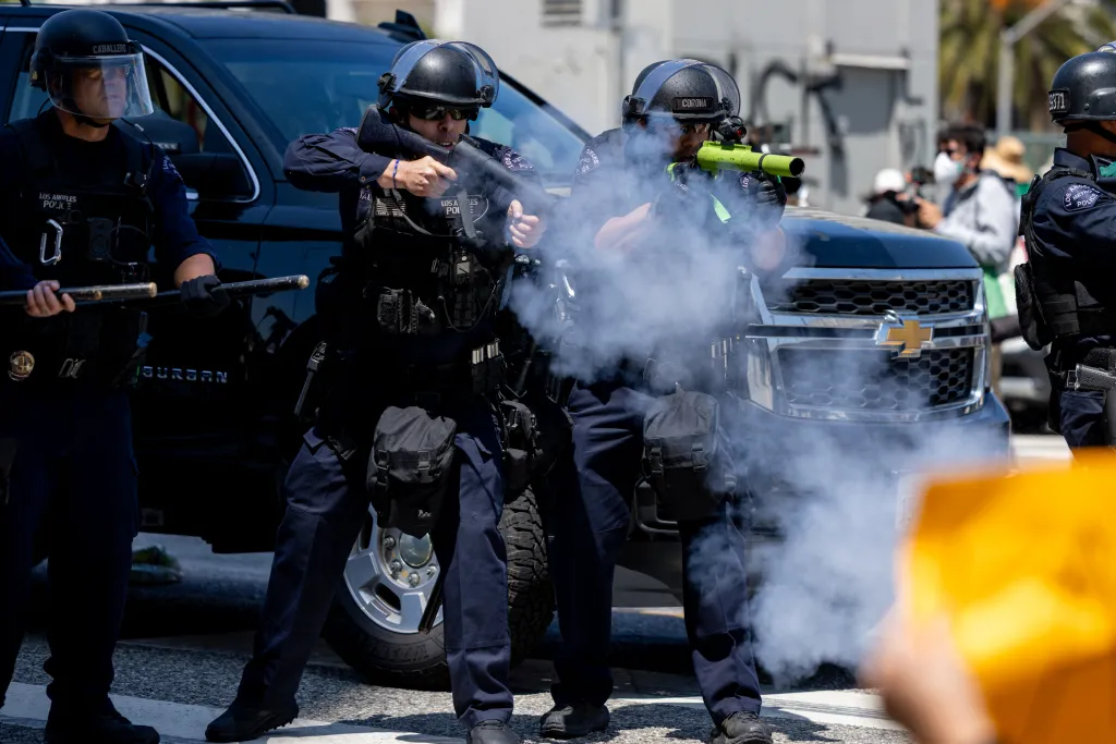 Police officers fire rubber bullets, creating a cloud of smoke during an anti-ICE protest in Los Angeles.