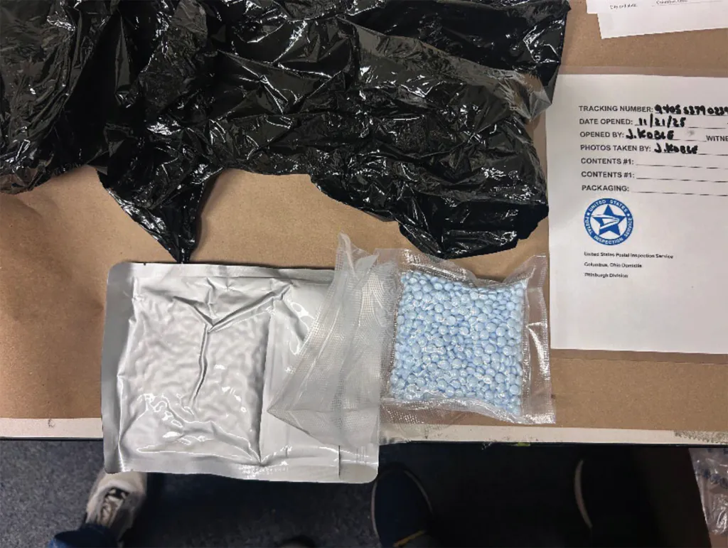 Opened parcel showing a black plastic bag, a silver vacuum-sealed bag, and a clear plastic bag containing numerous blue pills.