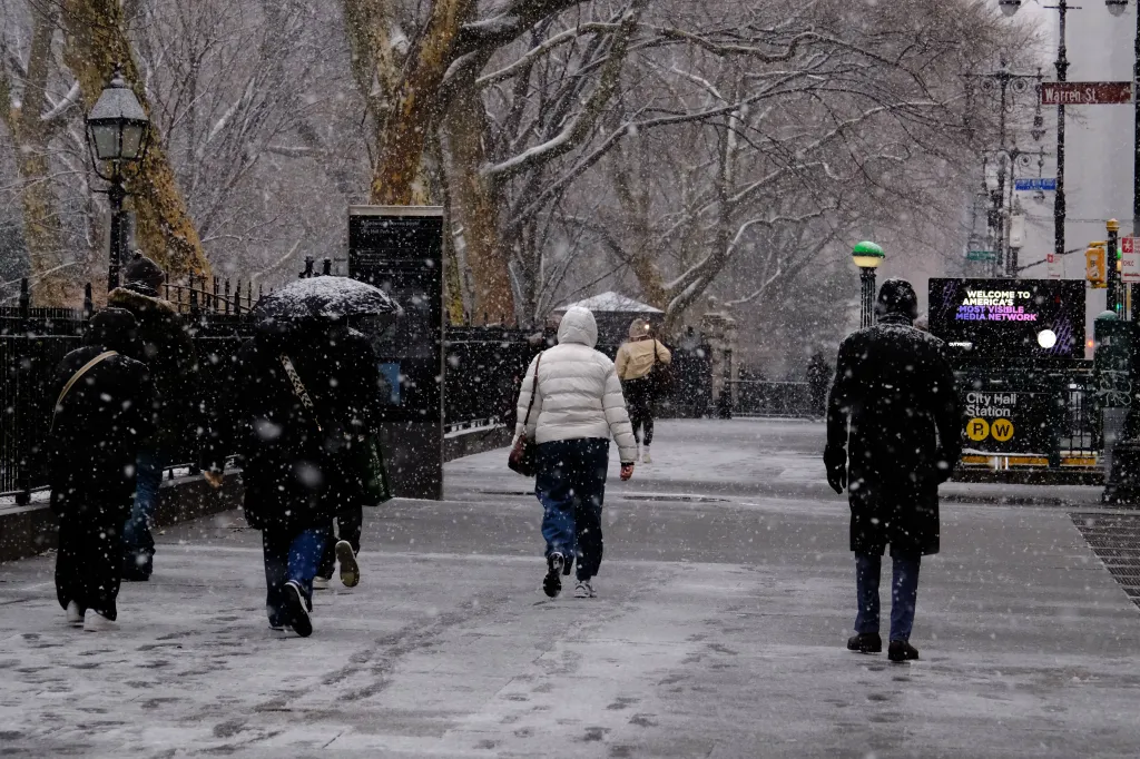 Snow falls on a street with pedestrians near City Hall Park in New York.