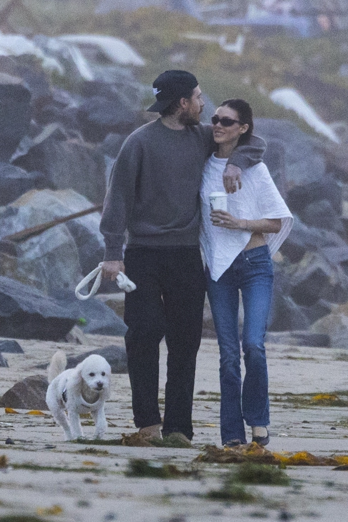 Brooklyn Beckham and Nicola Peltz Beckham walking on a beach with their white rescue dog.