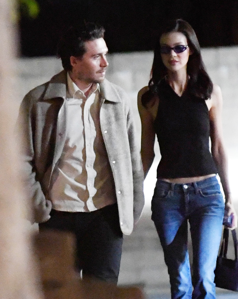 Brooklyn Beckham and Nicola Peltz walking together, with Beckham wearing a cardigan and Peltz in a black halter top and skinny jeans.