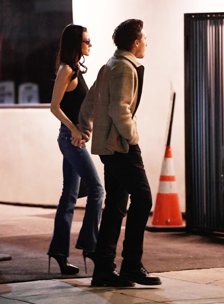 Brooklyn Beckham in a cardigan and Nicola Peltz in a black halter top and skinny jeans walking together.