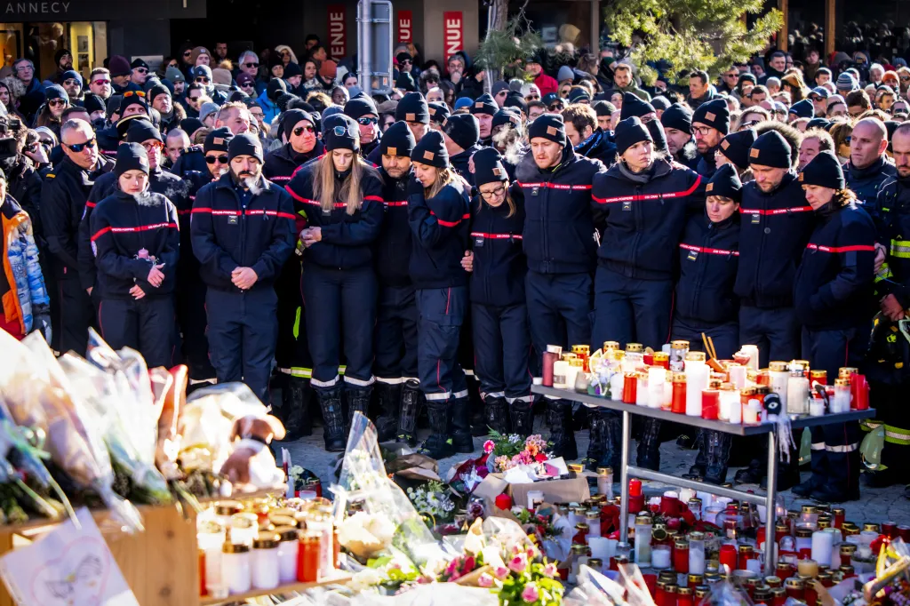 Firefighters gather around a makeshift memorial with flowers and candles in Crans-Montana to pay respects to victims of a fire.