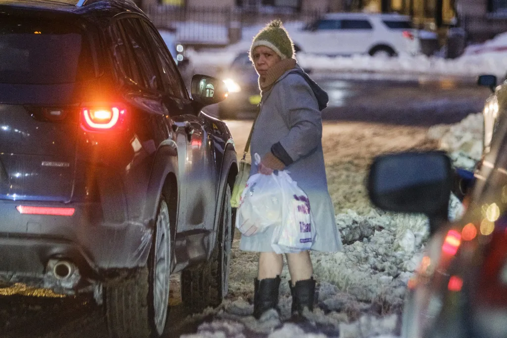 Lissette Soto Domenech holding plastic bags next to a car on a snowy street.