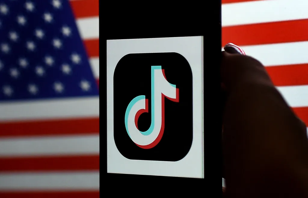 Illustration of the TikTok app logo on a phone screen, overlaid on a blurred American flag.