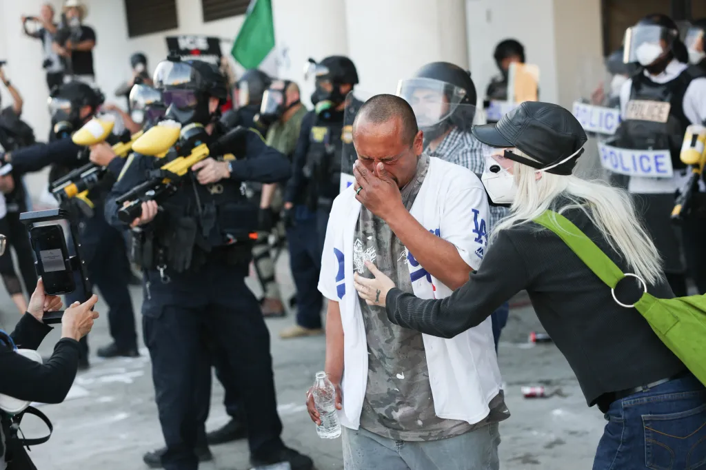 A man reacts to being gassed by police during a protest, holding his hand to his face as a woman comforts him.
