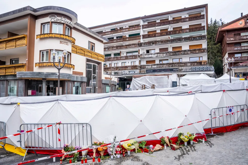Tents set up around the Constellation bar in Crans-Montana, Switzerland after a fire, with flowers and candles laid in tribute.