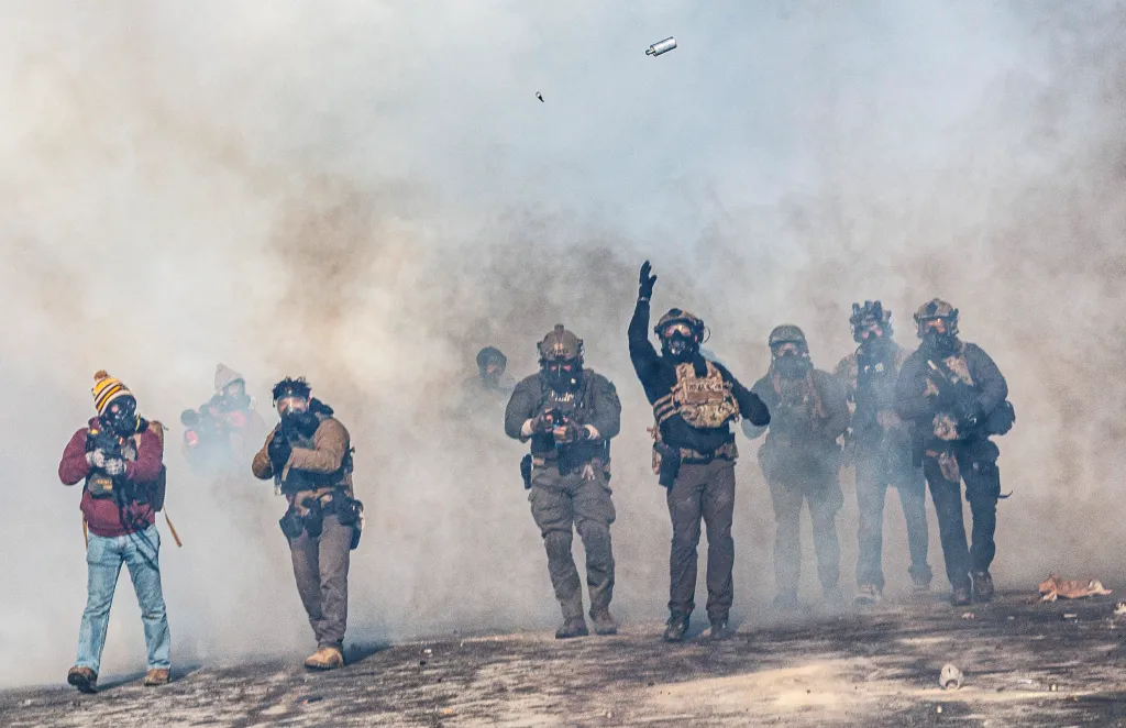 Federal agents advance through tear gas, one launching a tear gas canister.