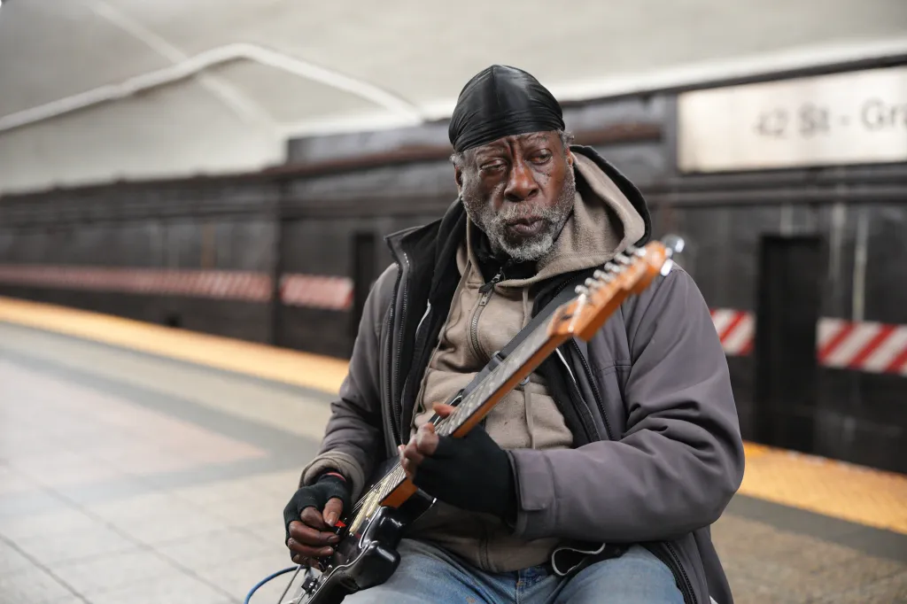 David Spectra, 71, of the Bronx, plays an electric guitar in a subway station with a sign for 42 St - Grand in the background.