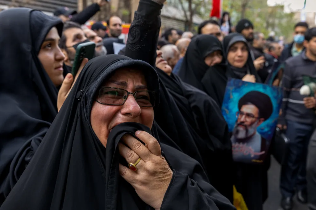 A woman wearing a black chador and glasses cries, holding a hand to her mouth, at a mass funeral for security forces in Tehran.