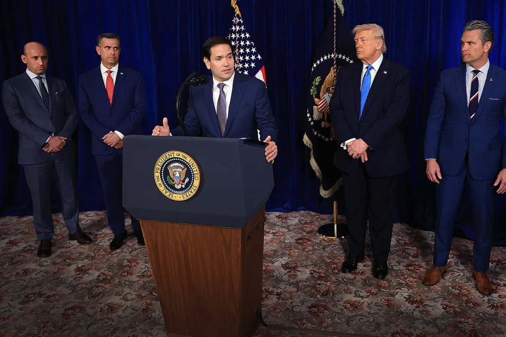 Secretary of State Marco Rubio speaks at a podium with Homeland Security Advisor Stephen Miller, CIA Director John Ratcliffe, President Donald Trump, Secretary of War Pete Hegseth, and Chairman of the Joint Chiefs of Staff Dan Caine standing behind him.