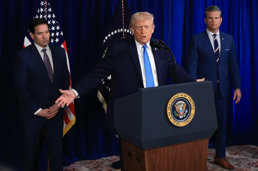 President Trump speaks at a podium with the Seal of the President, flanked by Secretary of State Marco Rubio and Secretary of War Pete Hegseth.