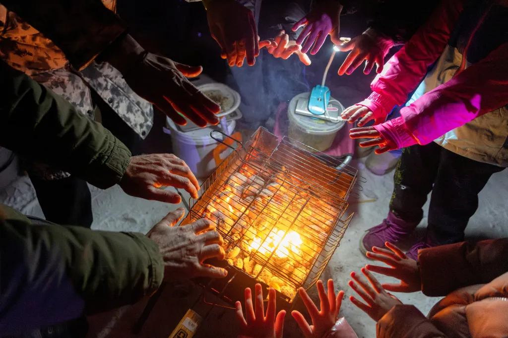 People warm their hands over a BBQ during a blackout party in Kyiv, after losing electricity from a Russian drone and airstrike on Jan. 24, 2026.