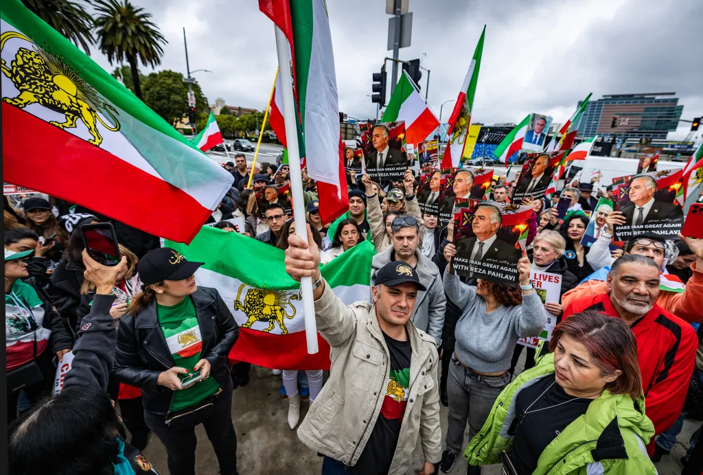 Protesters holding Iranian flags and signs supporting Reza Pahlavi.