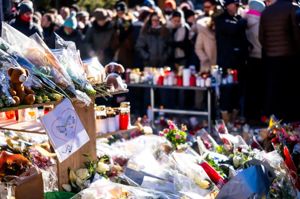 Makeshift memorial near a bar in Crans-Montana with flowers, messages, stuffed animals, and candles.