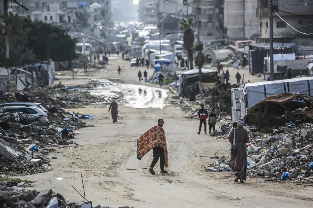 A man carrying a mattress walks along a road amid destroyed buildings in Jabalia, in the northern Gaza Strip.