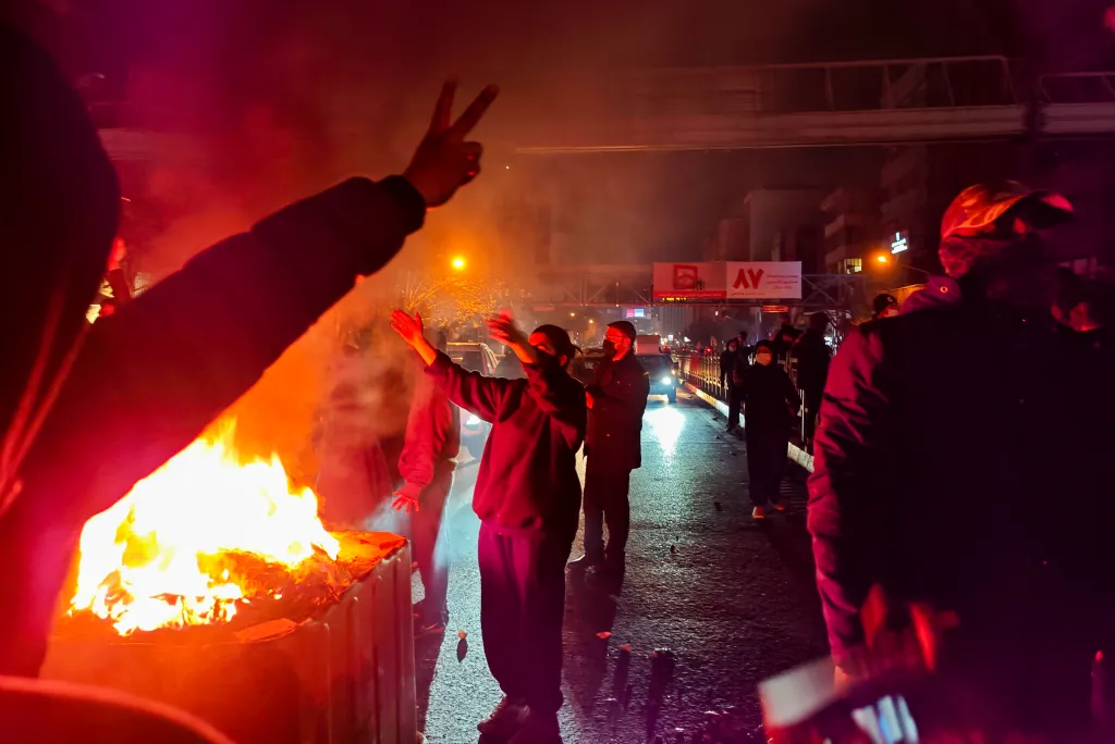Iranians protesting near cars set on fire in a street in Tehran.