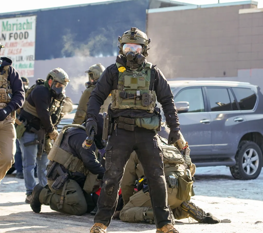 Federal agents in tactical gear, including gas masks, confront protesters following a fatal shooting in Minneapolis.