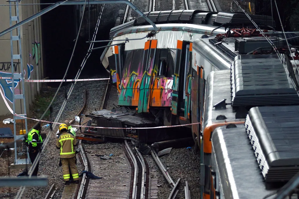 Two emergency responders near a derailed commuter train covered in graffiti, next to an overhead bridge.
