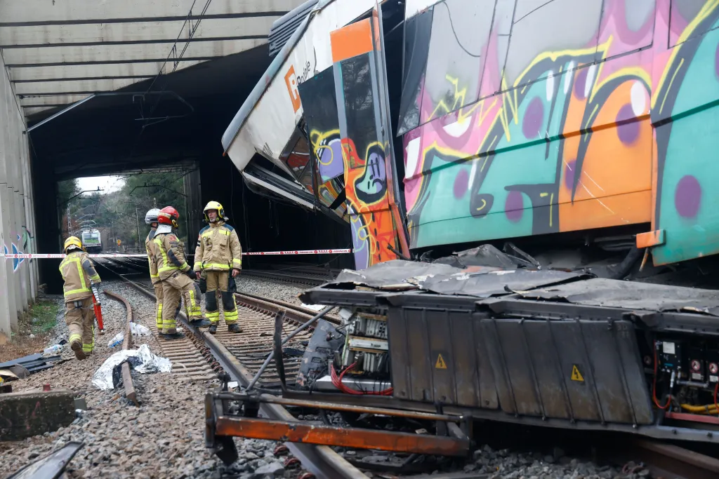 Rescuers inspect a derailed train with graffiti on its side, next to a collapsed retaining wall.