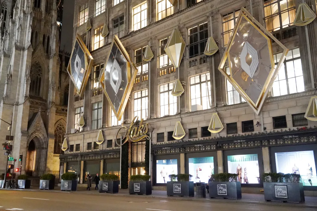 Exterior of the Saks Fifth Avenue flagship store at night, decorated with large diamond-shaped lights and smaller pendant lights.