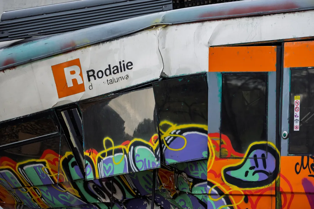 The side of a derailed Rodalie train in Gelida, Spain, covered in graffiti, showing damage to its driver's cab.