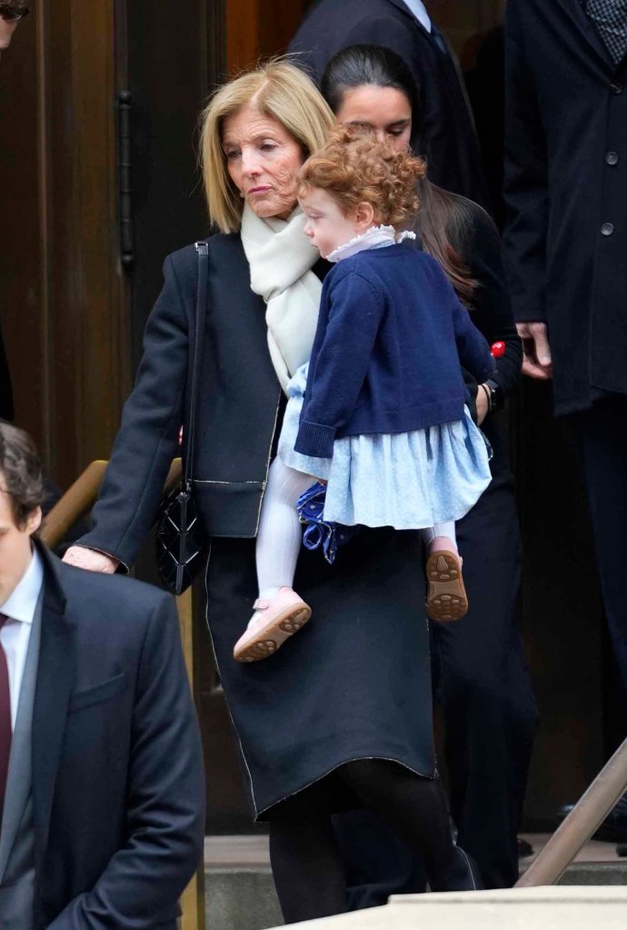 Caroline Kennedy, in a black coat and cream scarf, carrying Josephine Moran, in a blue cardigan and blue dress.