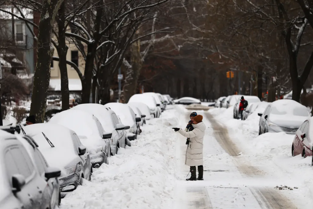 A woman and child walk in a snow covered street in Brooklyn after a storm left nearly one foot of snow on January 26, 2026 in New York City.