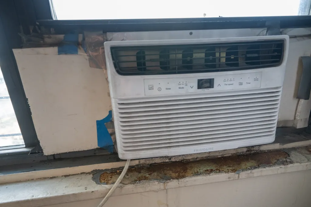 A Frigidaire air conditioner unit in a window, with insulation and blue tape visible around it.