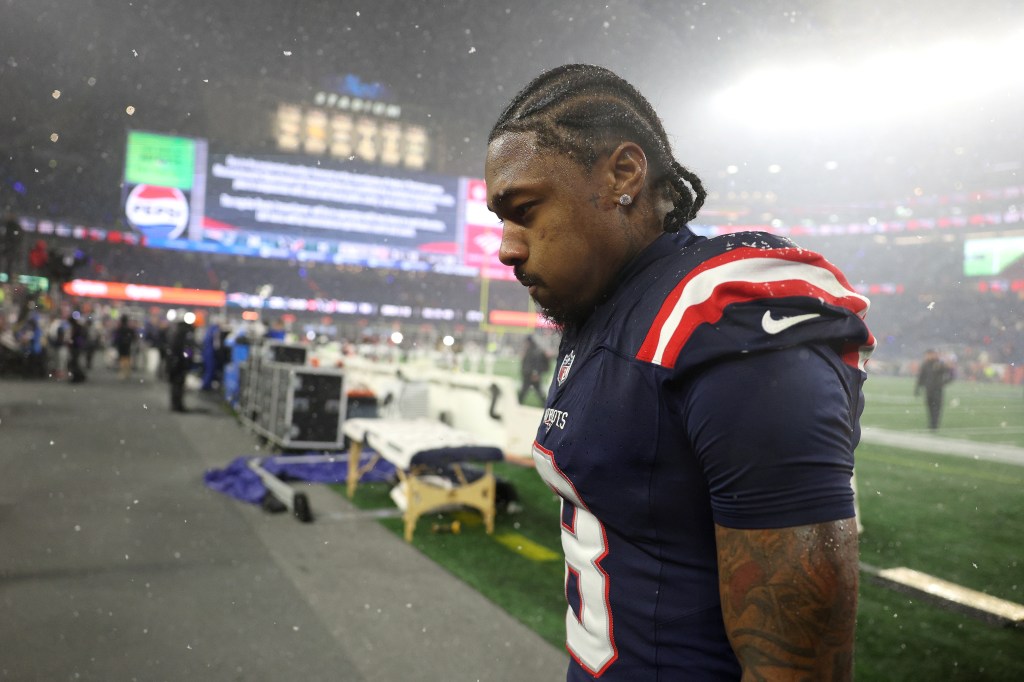 Stefon Diggs, wearing a New England Patriots jersey, walks off the field in the snow after a game.