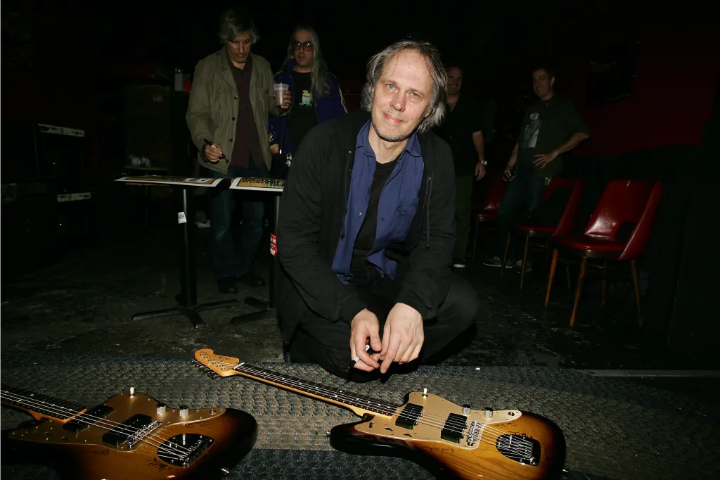 A man crouching on the floor next to two Fender Jazzmaster guitars at the 50th Anniversary Concert.