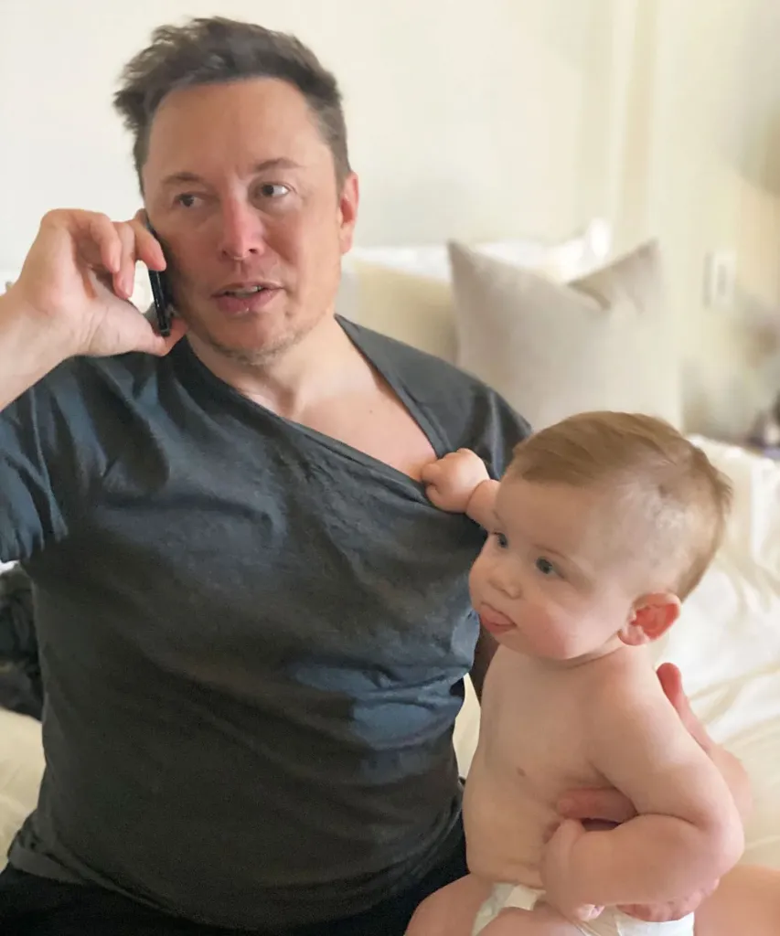 Elon Musk holding his baby while talking on a phone.