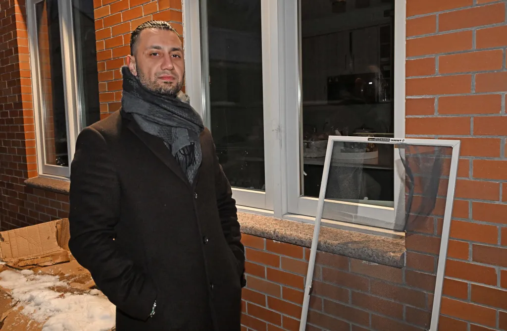 Moshe Borukh stands outside his home next to a window screen removed by thieves.