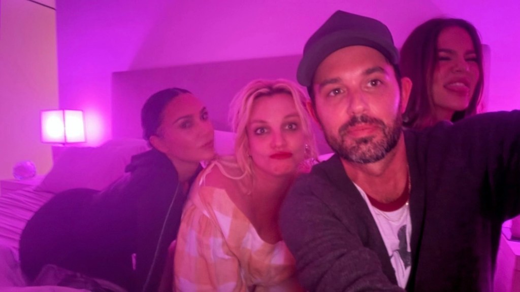 Kim and Khloé Kardashian, Britney Spears, and Cade Hudson pose for a selfie under pink lighting.