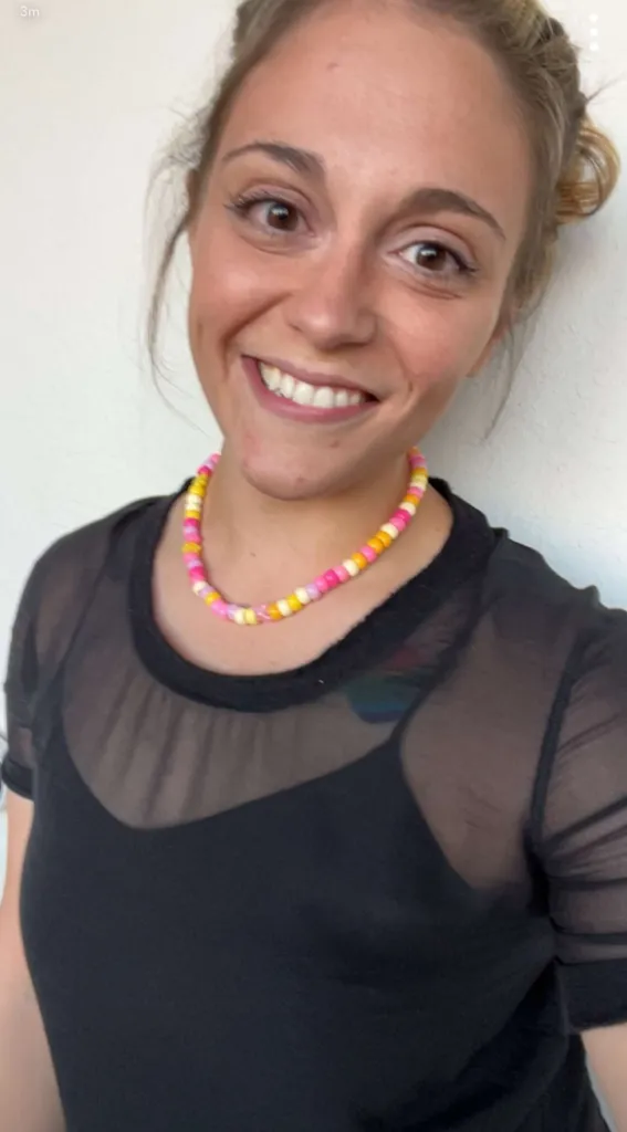 A smiling woman wearing a colorful bead necklace and a sheer black top.