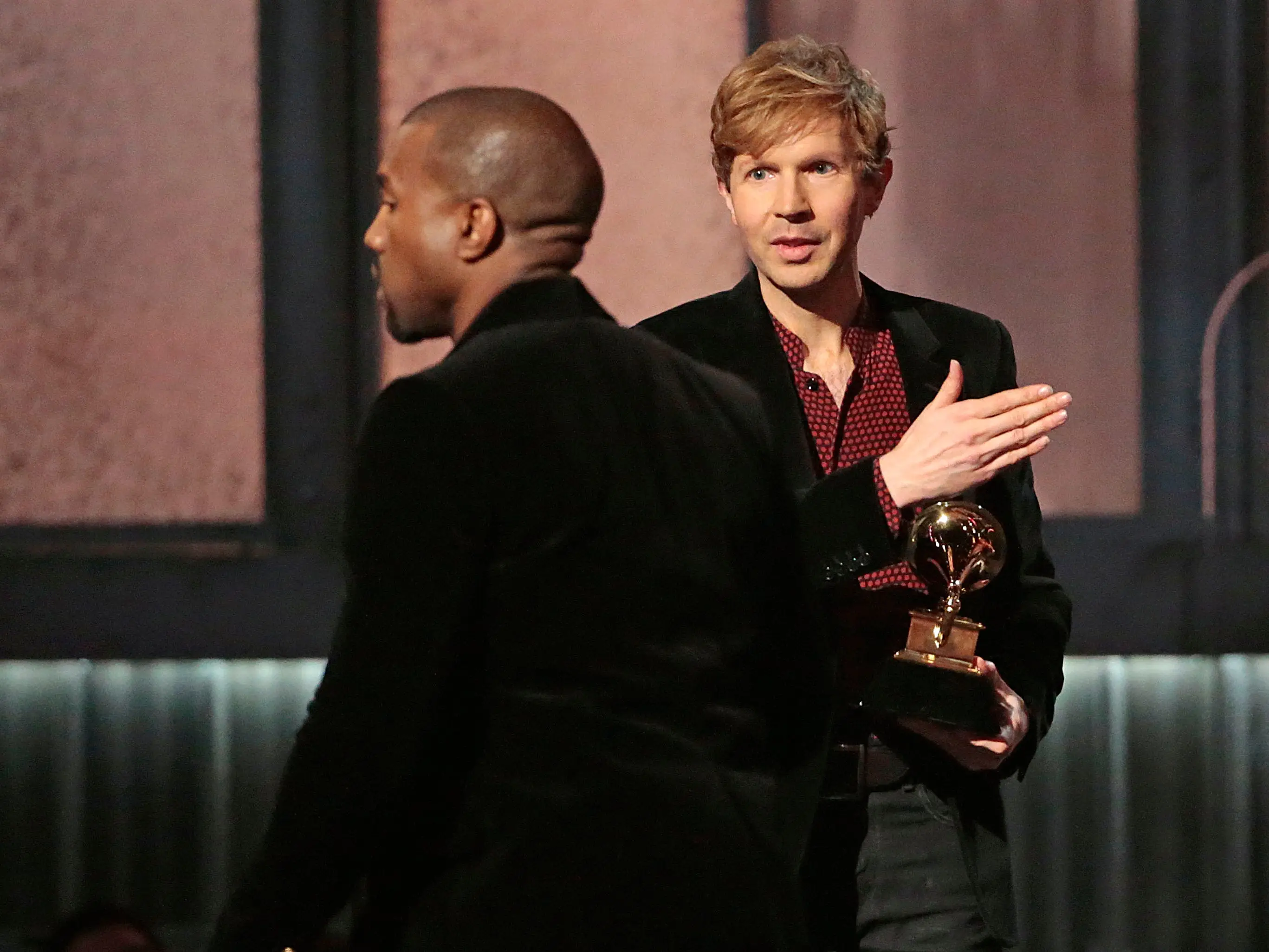 Kanye walking across stage while Beck holds his award and his hand up ready to defend himself.