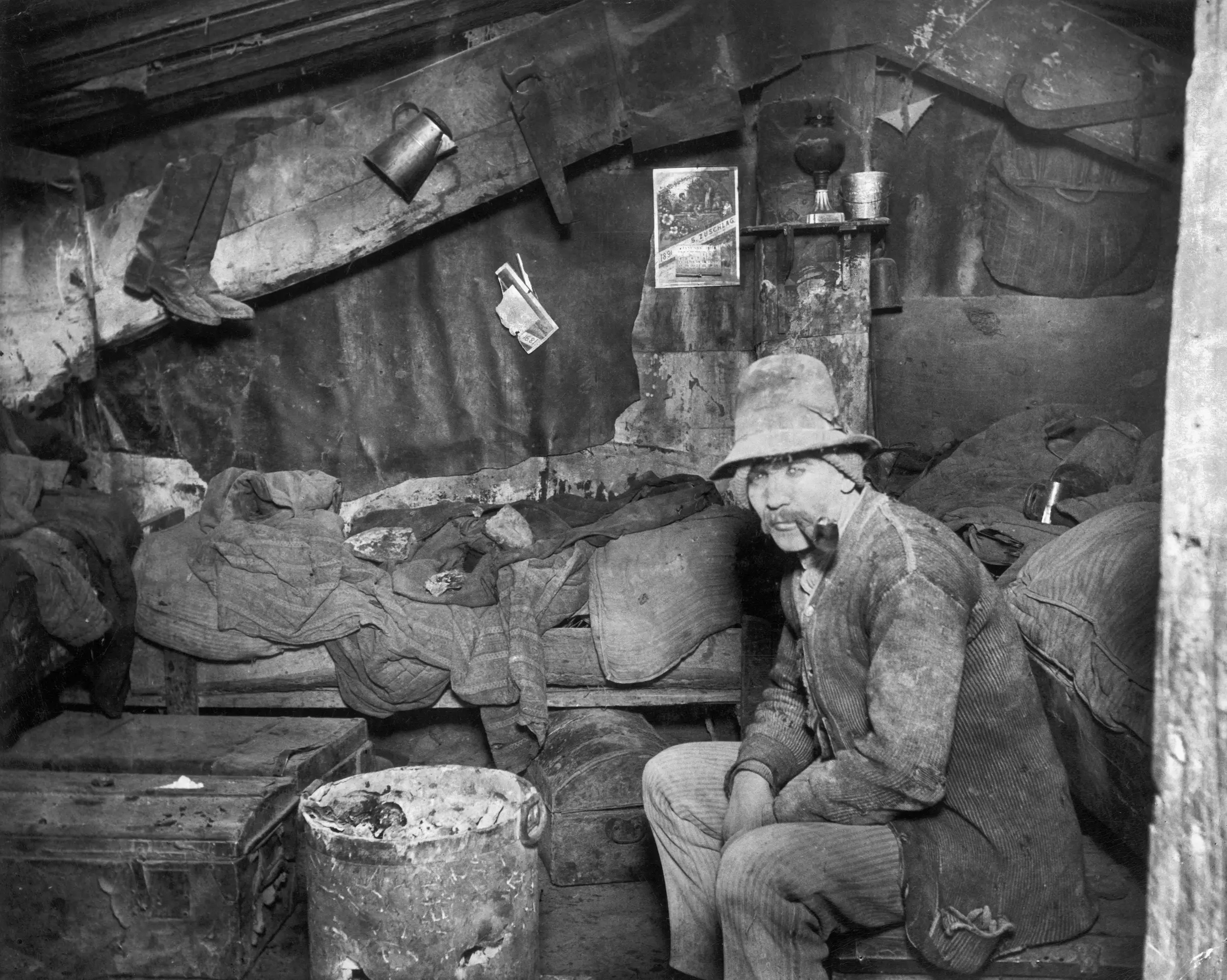 A photo shows a man smoking a pipe in his living quarters in the cellar of a New York City tenement house in 1891.