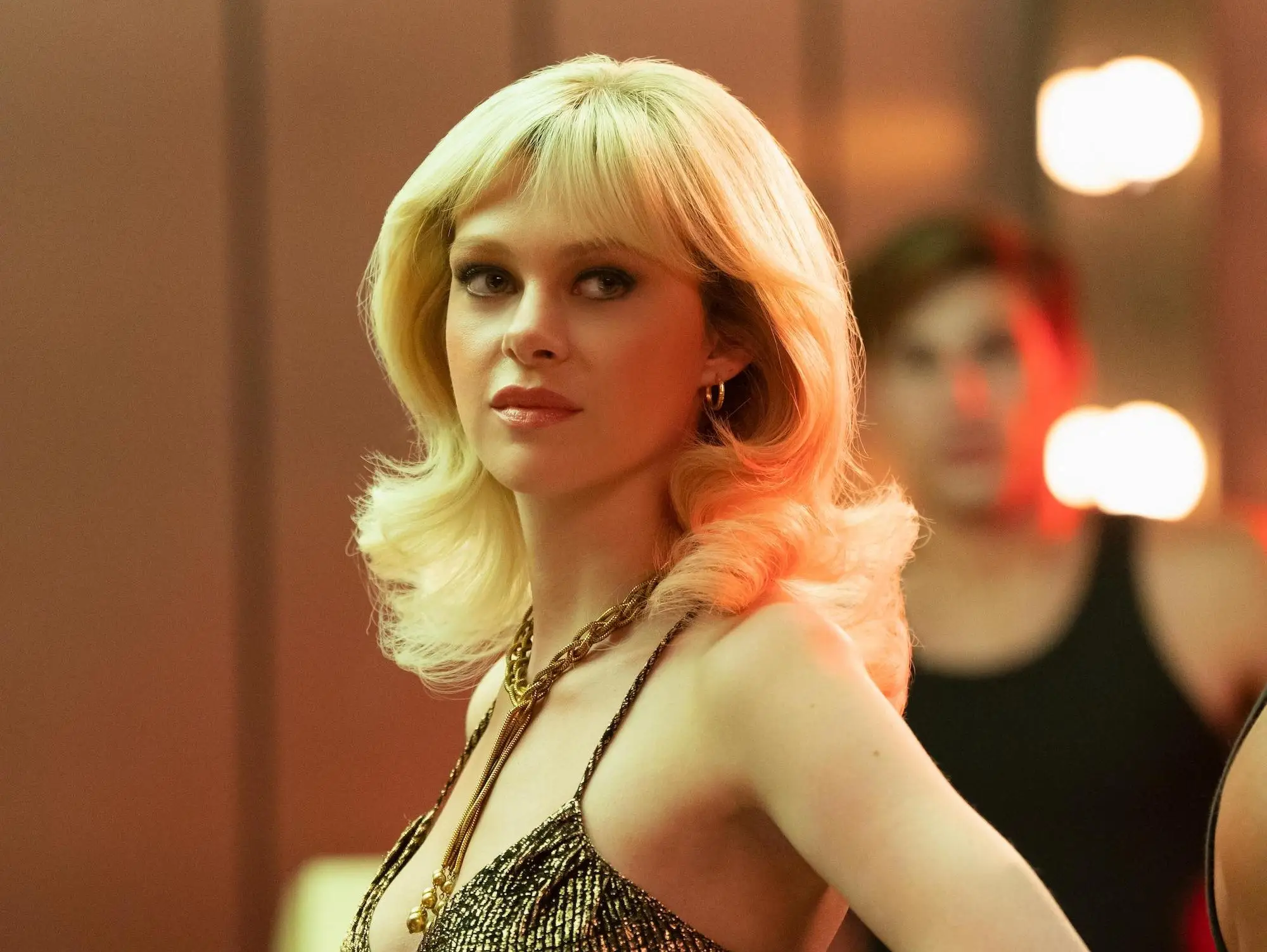 Dorothy Stratten stands near the bar in a gold dress in this still from 