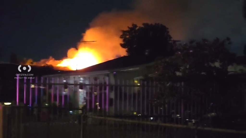 Nighttime photo of an apartment building with large flames and smoke rising from its roof.