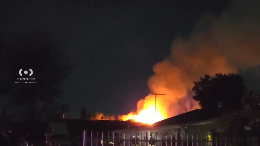 A building on Purdy Avenue in Bell Gardens on fire, with bright orange flames and smoke visible against the dark night sky.
