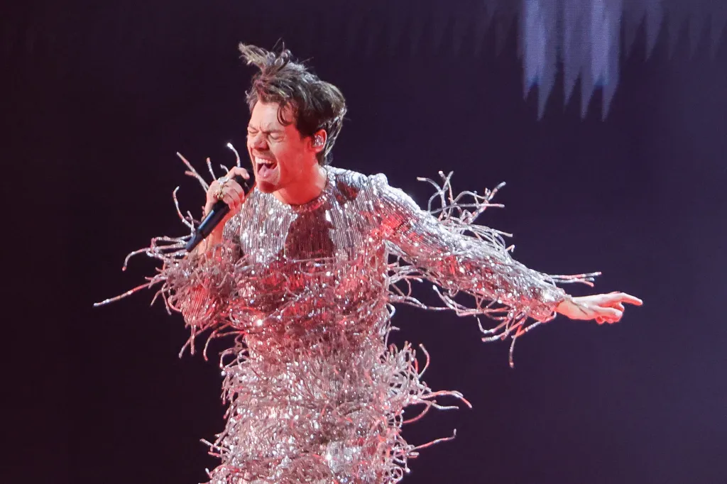 Harry Styles performing at the Grammy Awards in a shimmering, fringed outfit, holding a microphone.