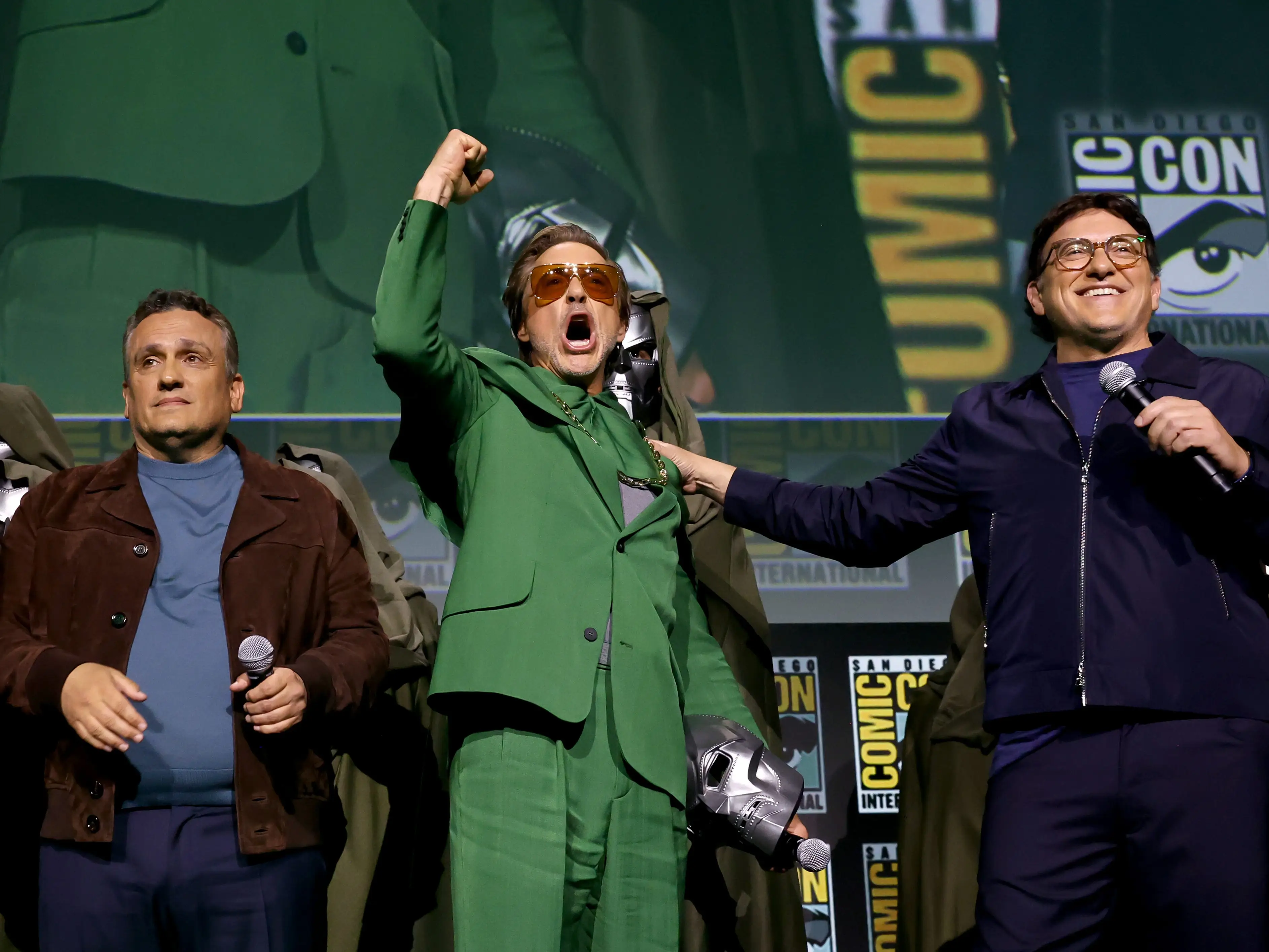 Joe Russo, Robert Downey Jr. with a fist raised up and Anthony Russo stand together at San Diego Comic Con in July 2024.