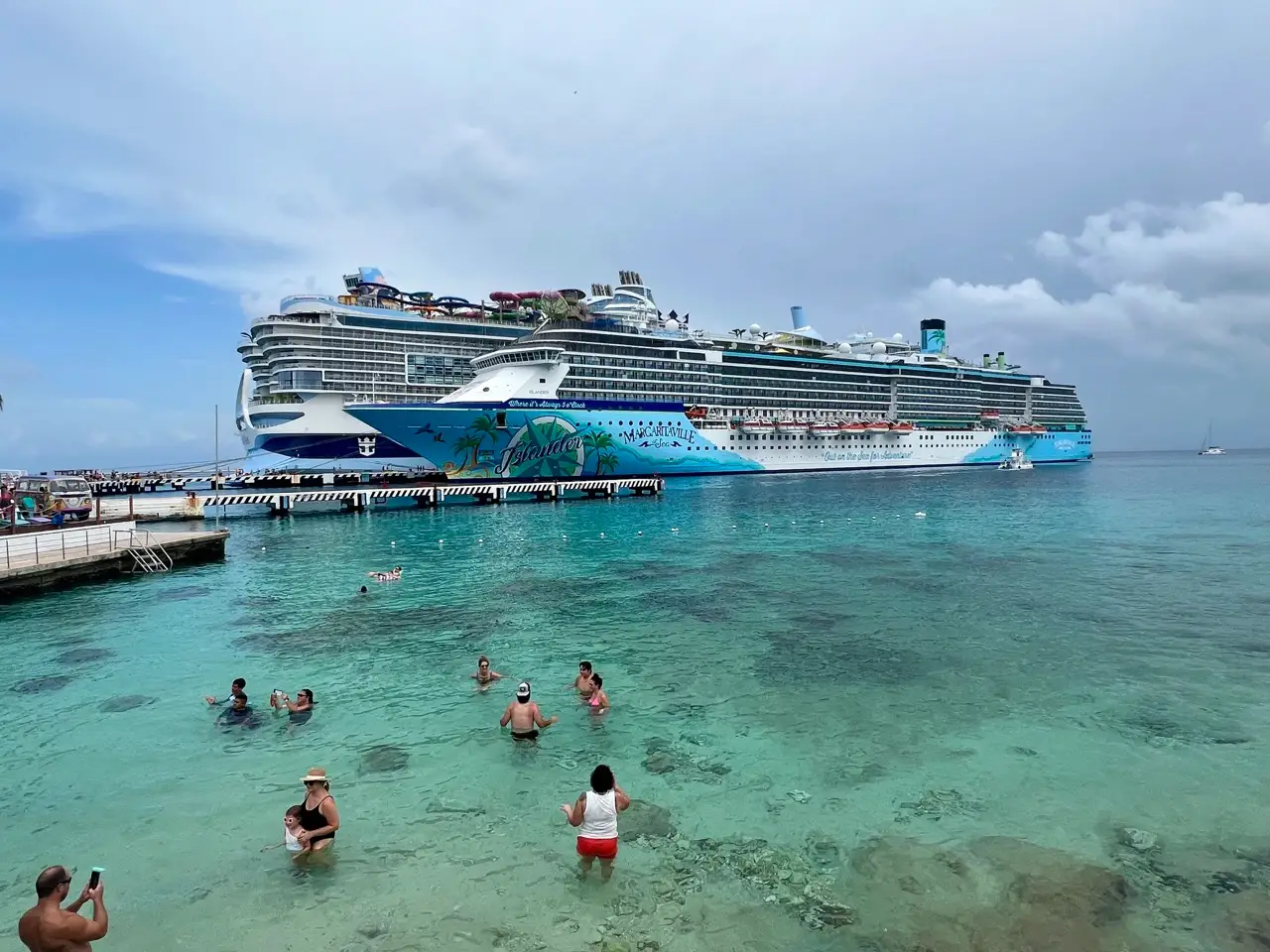 The Margaritaville Islander cruise ship docked at a port with people swimming in the sea.