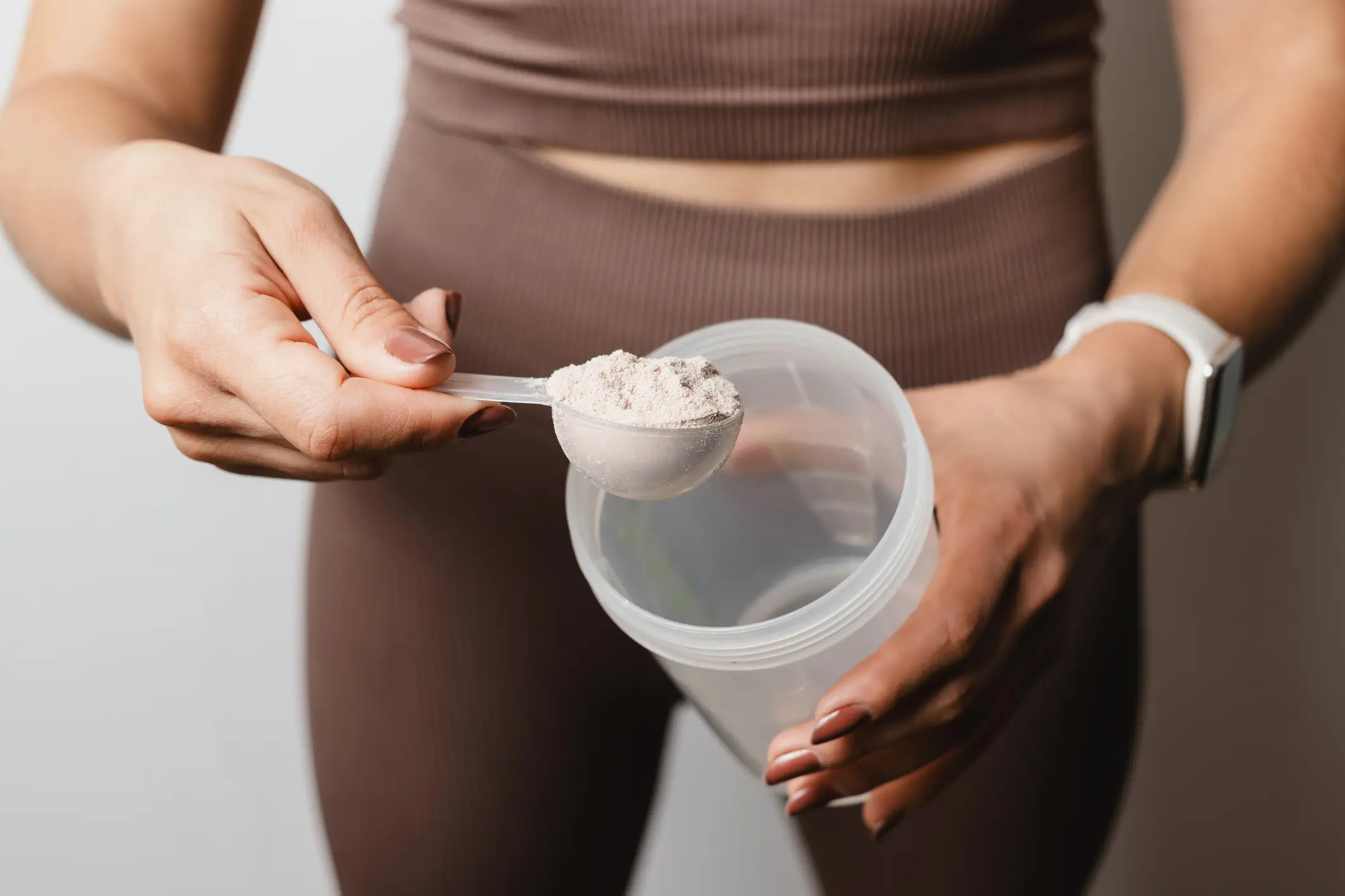 A person scooping a supplement powder into a clear plastic cup.