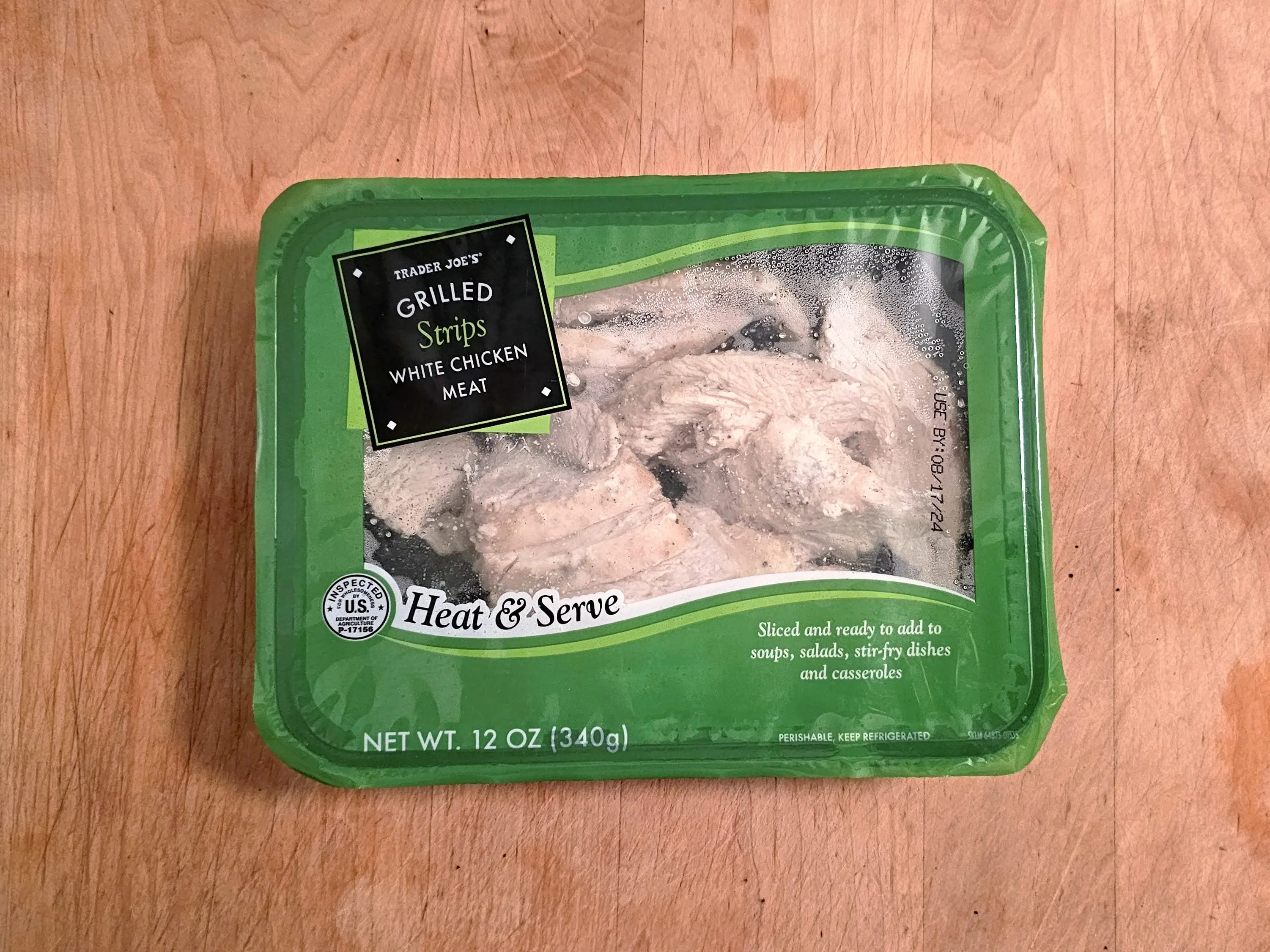 A packaged box of Trader Joe's white-chicken meat grilled strips on a wooden background.
