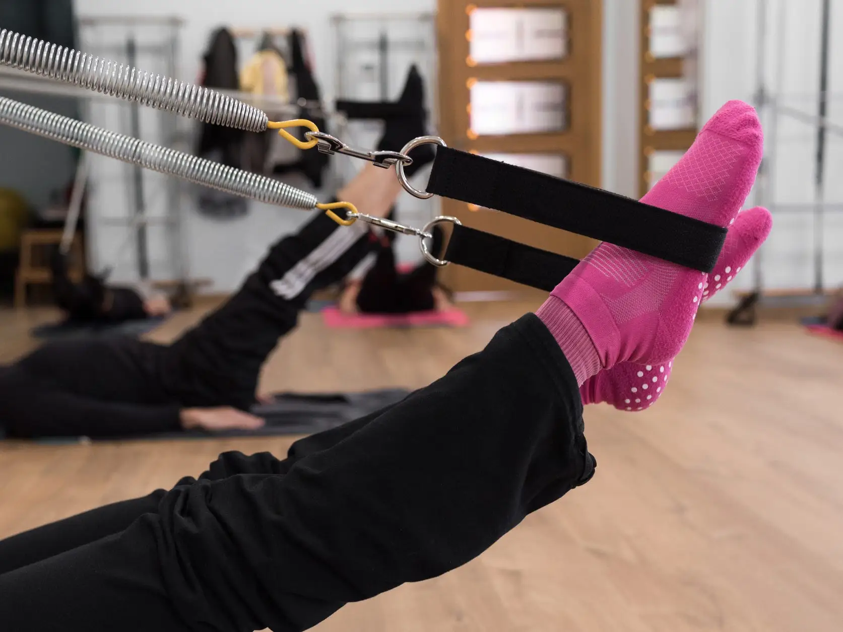 Legs in Pilates springs, wearing black pants and pink socks with grips at the bottom.