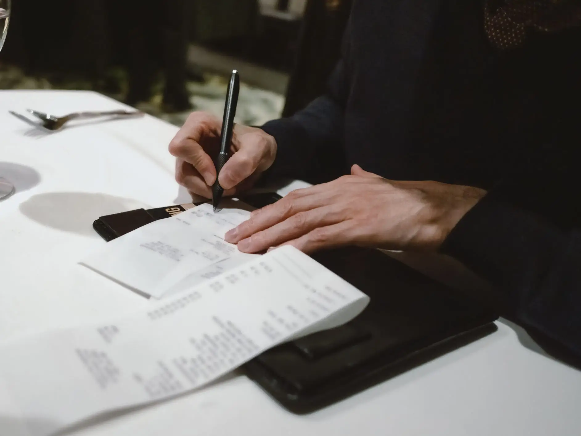 Close-up of a man writing in a tip on a credit-card receipt at a restaurant.