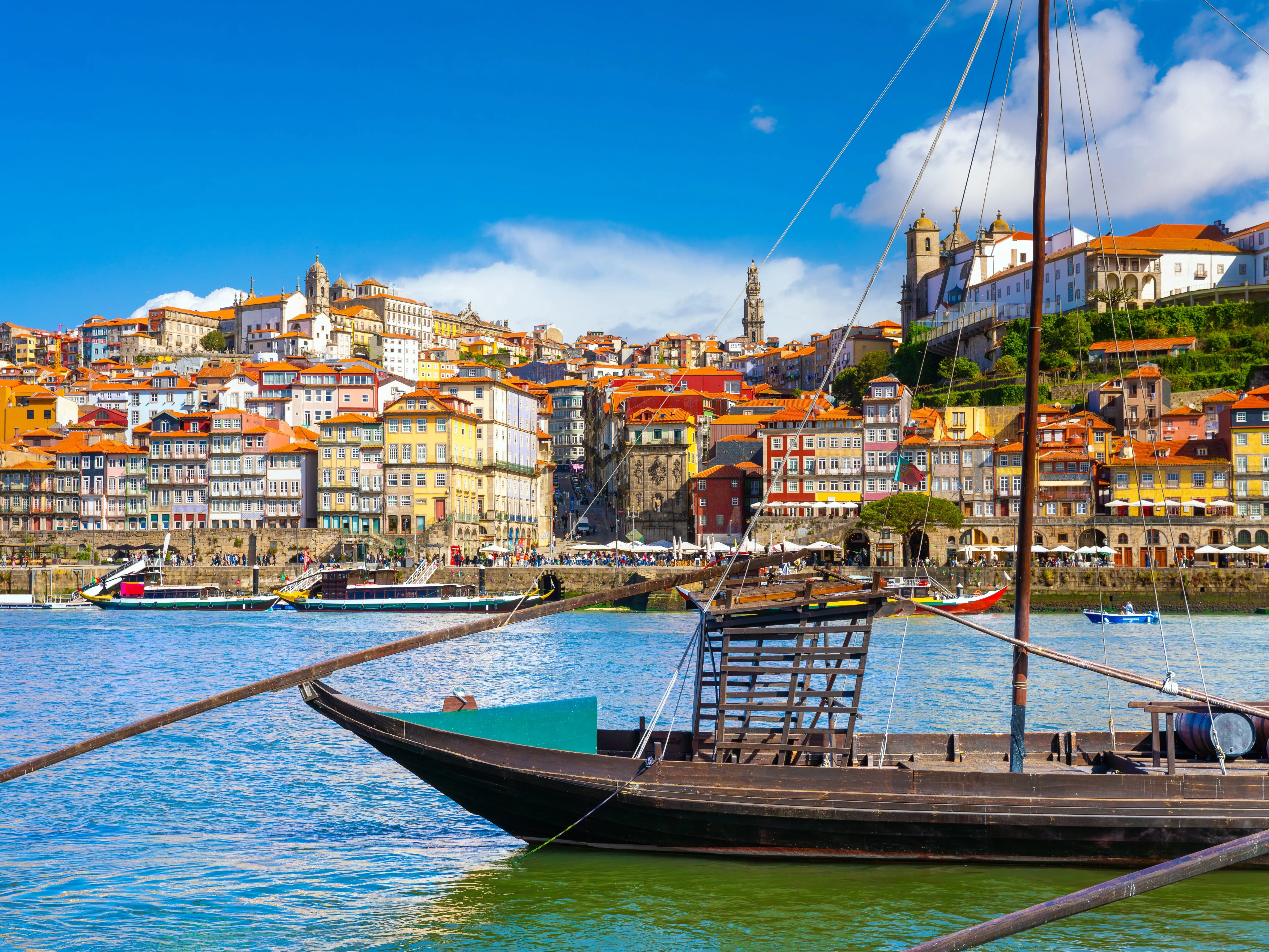 A ship in the water in front of a city with colorful buildings on a sunny day.